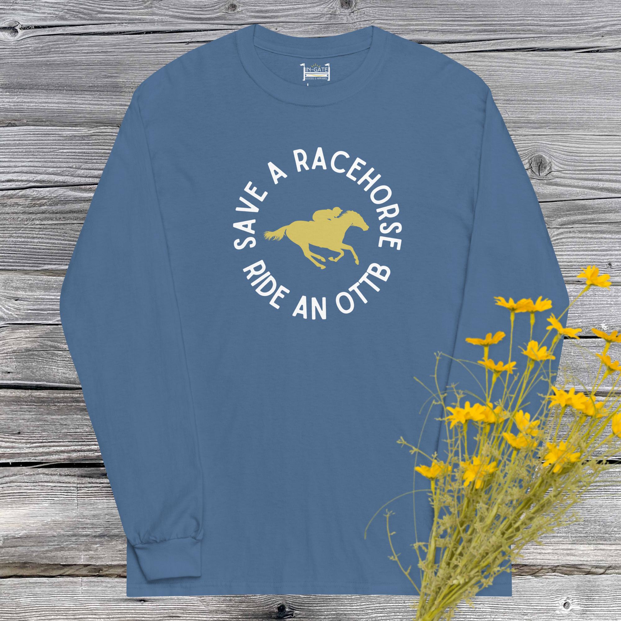 a long sleeve t-shirt in light blue with a circular save a racehorse, ride an OTTB logo with a yellow graphic of a jockey on a racehorse hanging in front of a weathered barn wood wall with yellow flowers in the corner